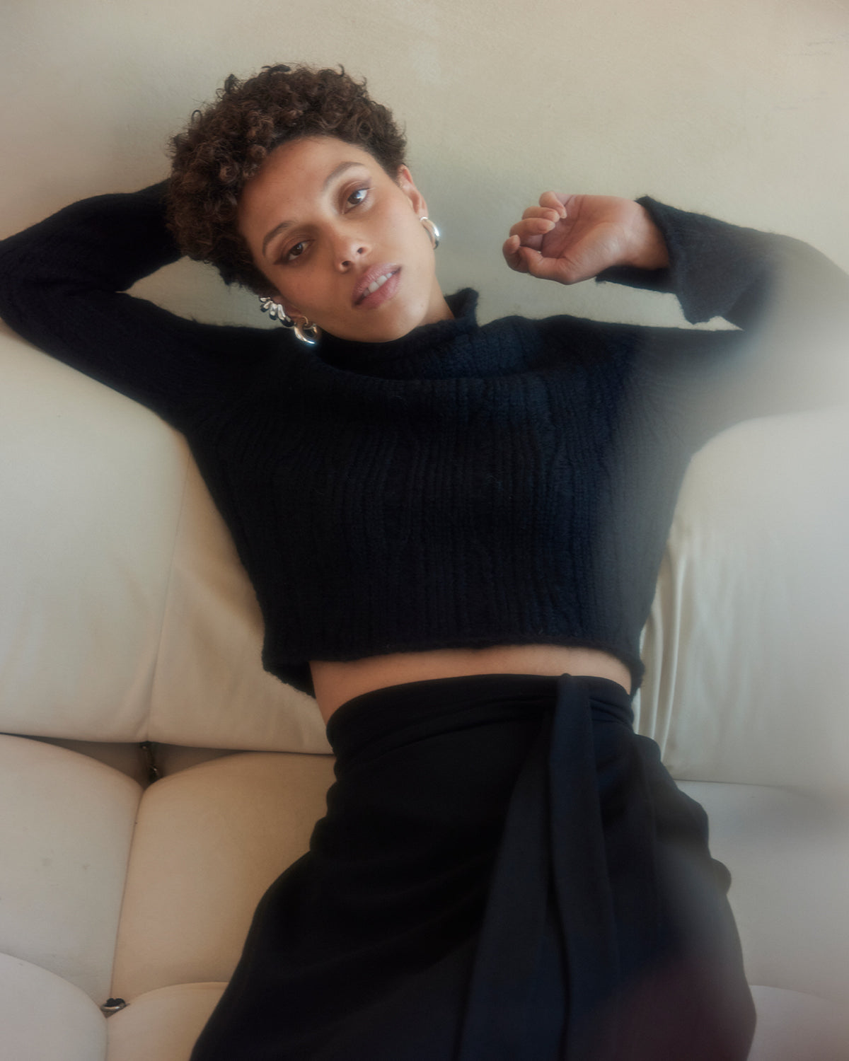 Person wearing a black sweater and pants sitting on a white couch.