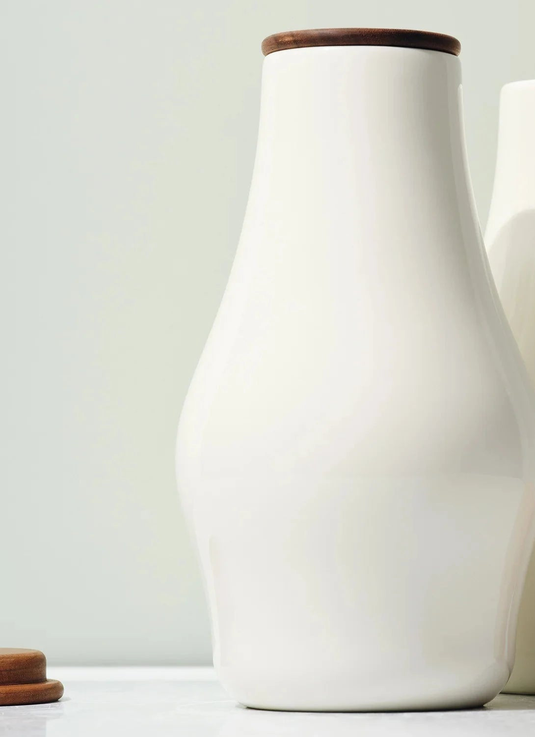 Two white ceramic bottles with wooden lids on a light background