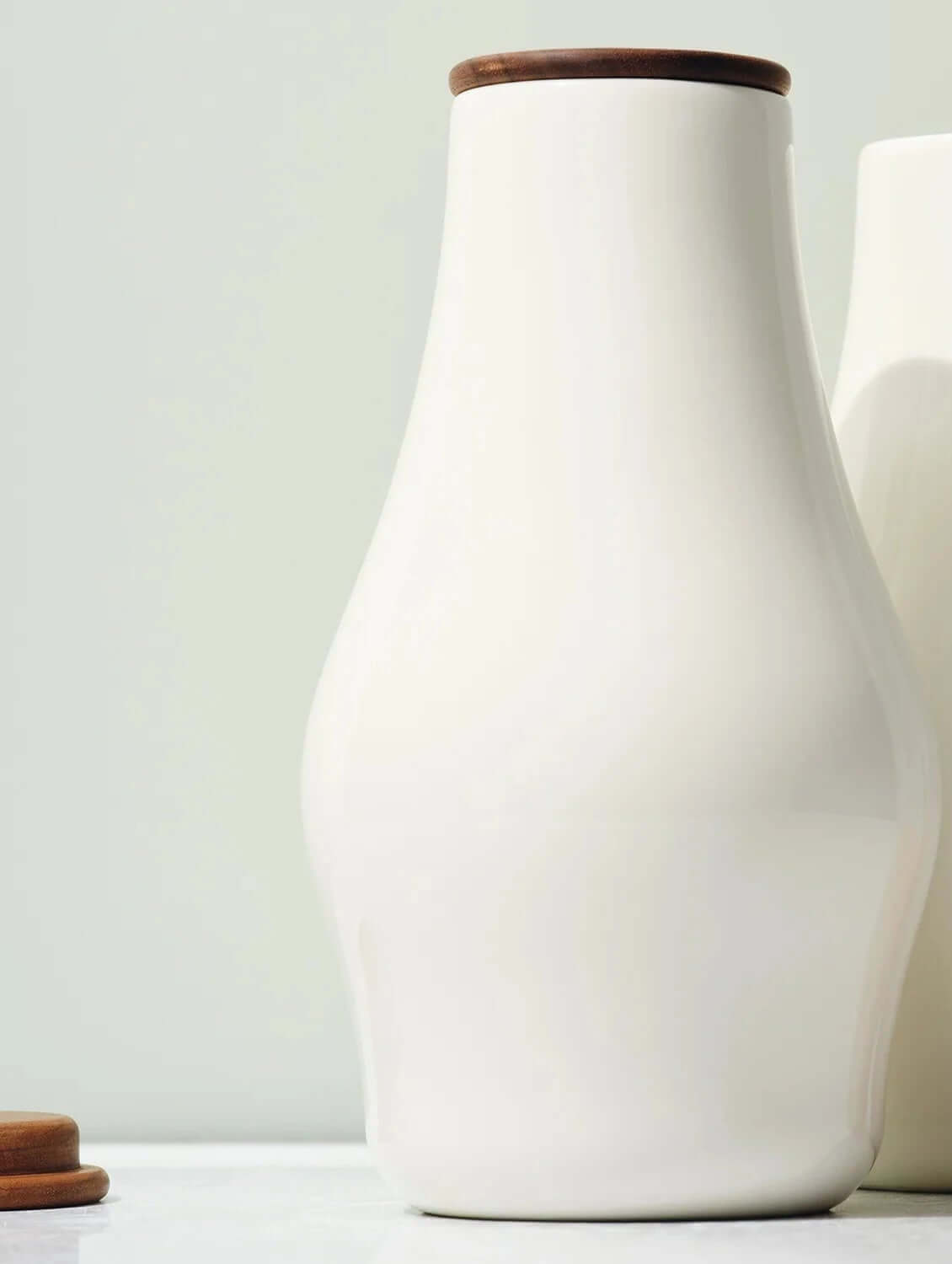 Two white ceramic bottles with wooden lids on a light background