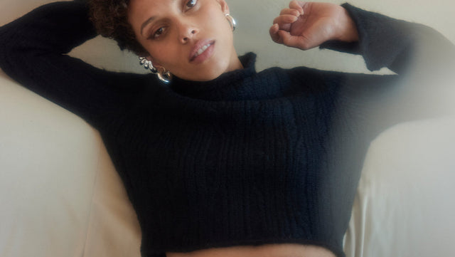 Person wearing a black sweater and pants sitting on a white couch.